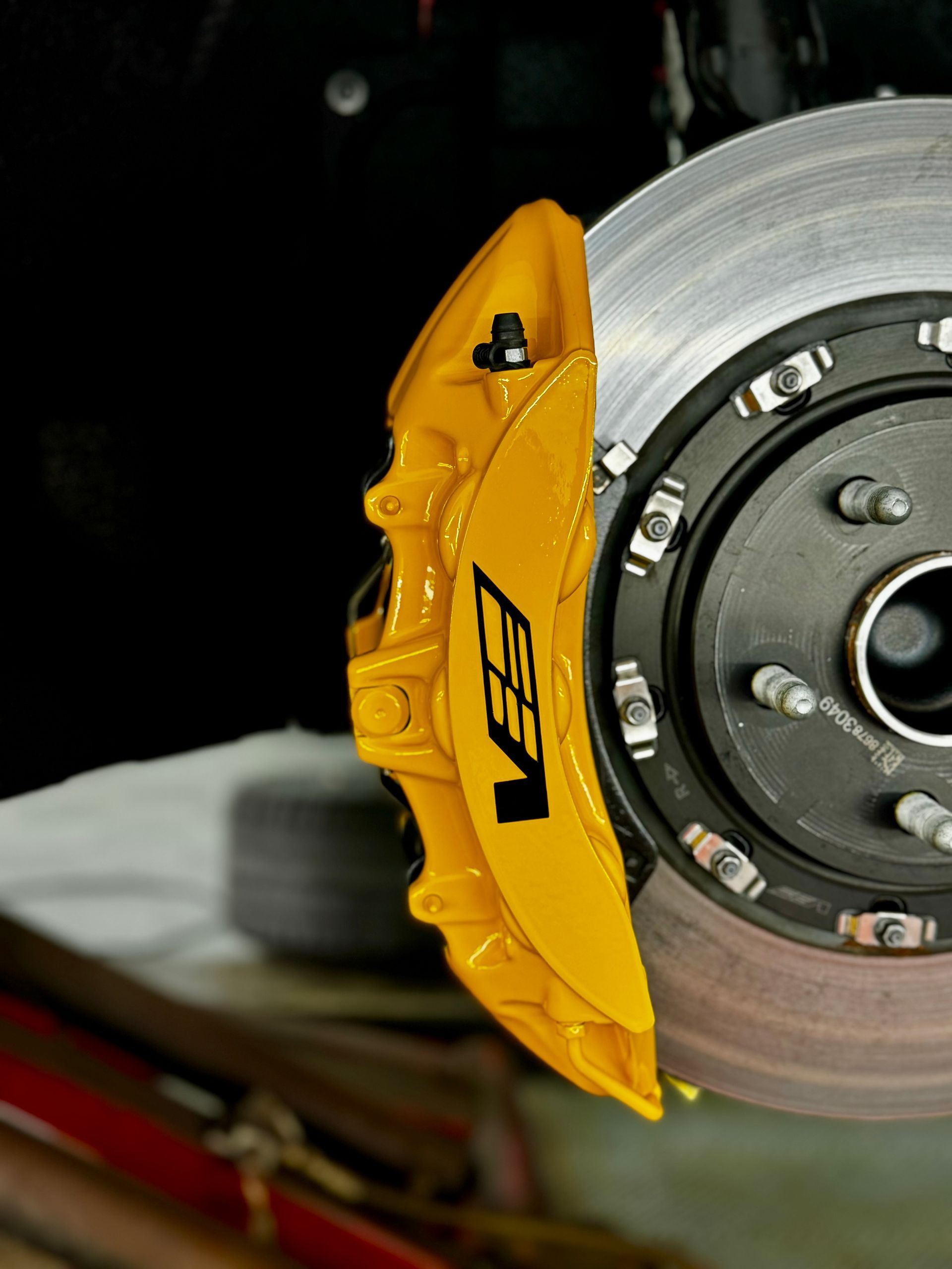 Close-up of a yellow VES caliper on a car brake rotor against a dark background