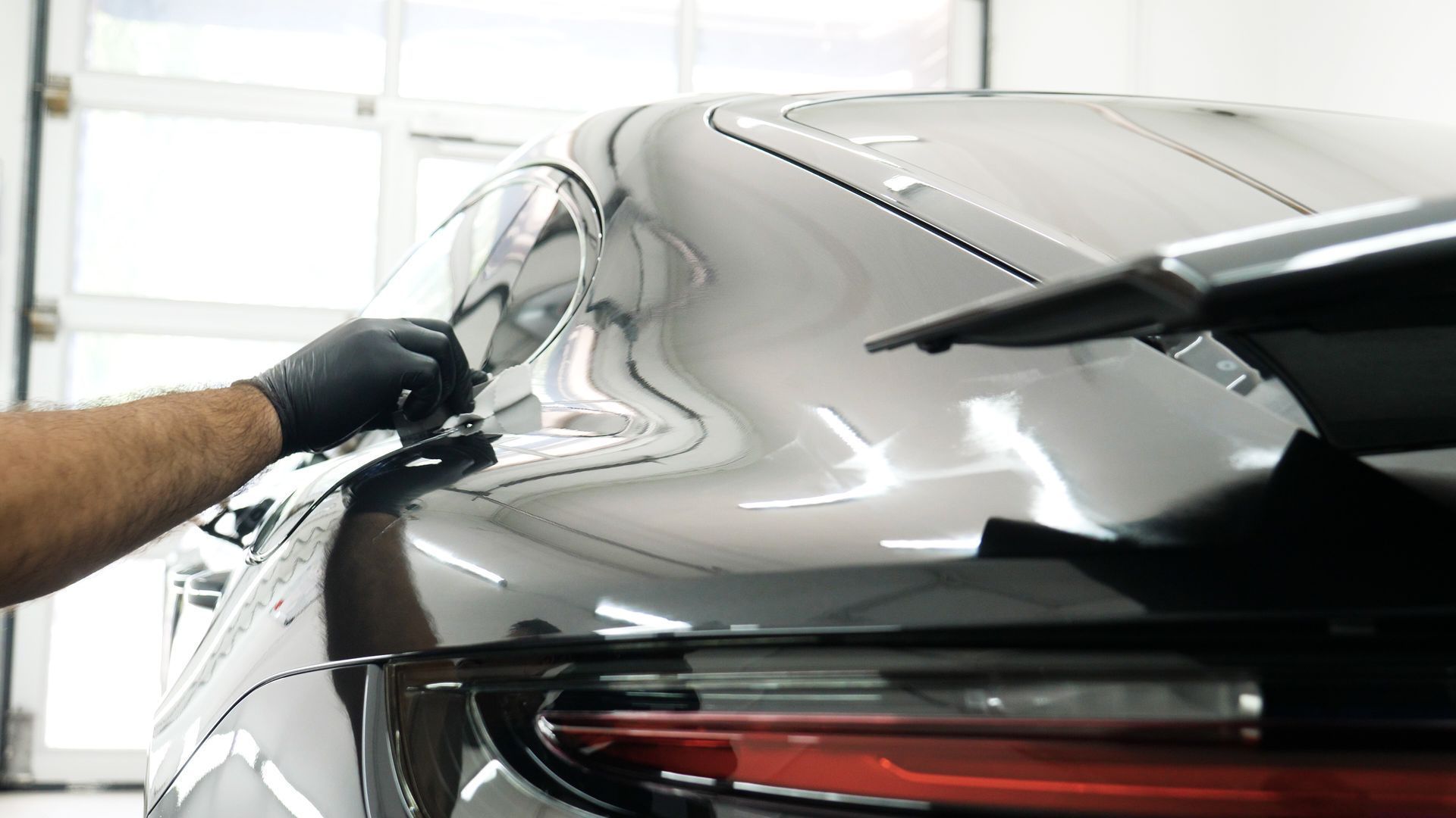 Gloved hand polishing a black car's rear quarter panel in a bright garage