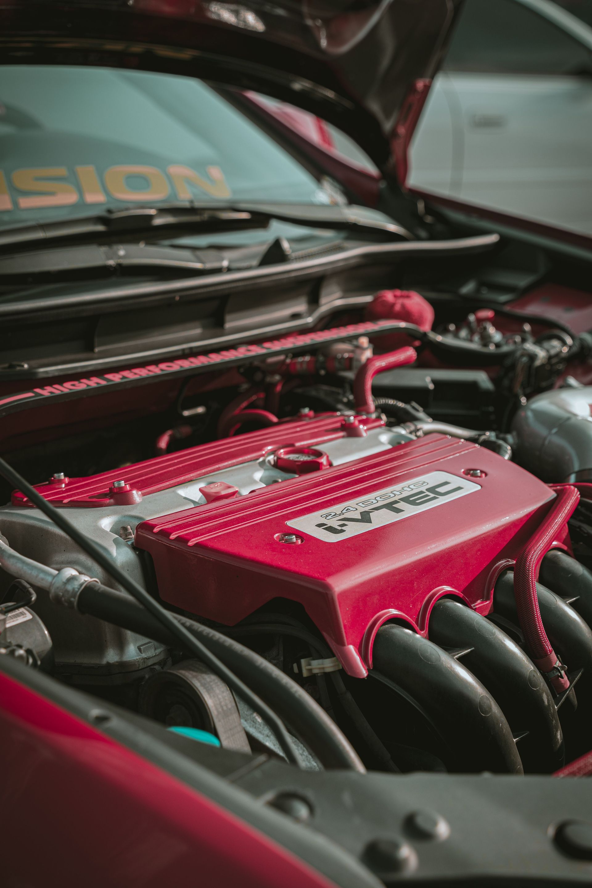 Red engine bay with a polished valve cover under an open car hood