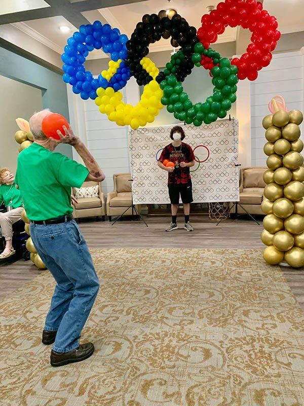 Man throws ball at Olympics-themed party, with Olympic rings made of balloons in the background.