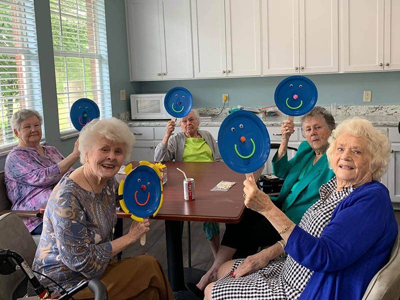 Group of seniors holding up blue paper plate smiley faces in a kitchen.