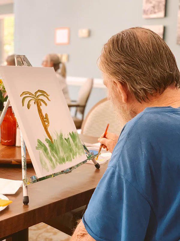 Person painting a palm tree on a canvas using a paintbrush.