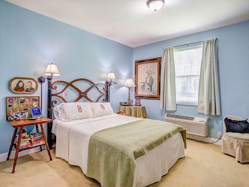 Bedroom with light blue walls, bed with green blanket, small side tables, and a window with curtains.