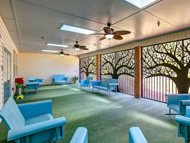 Covered outdoor seating area with blue furniture, decorative tree screens, and ceiling fans.