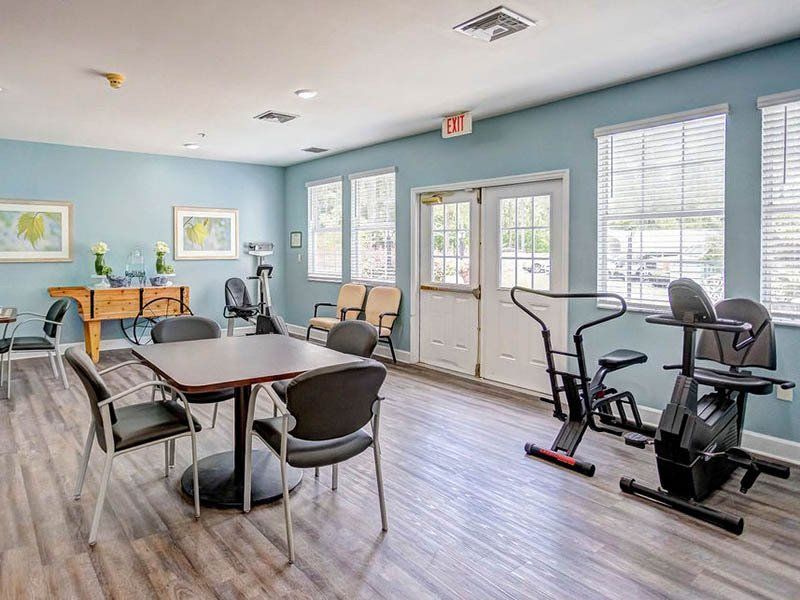 Gym with exercise equipment, table, chairs, windows, and door, blue walls, wooden floors.