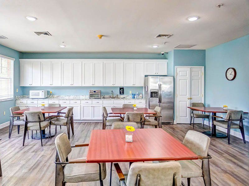 A dining room with red tables, chairs, white cabinets, and stainless steel refrigerator.