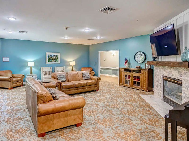 Spacious living room with leather sofas, fireplace, TV, and patterned carpet. Teal walls and warm lighting.