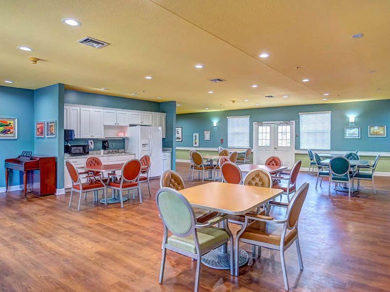 Dining hall with tables and chairs, kitchen area, wood floors, blue and yellow walls.