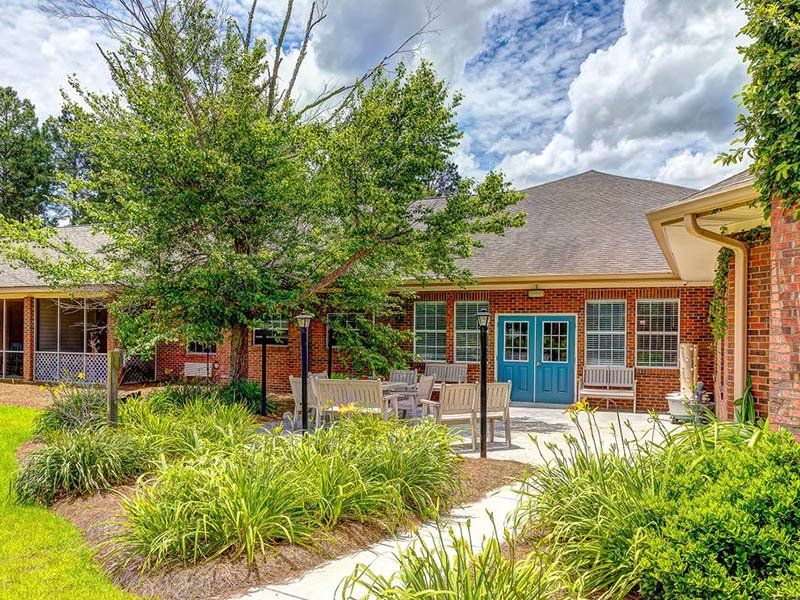 Exterior view of a brick building with a patio, benches, and landscaping; blue double doors.