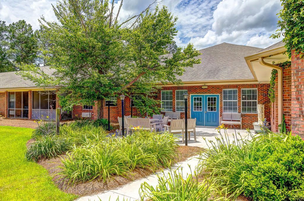 Exterior of a brick building with a garden, patio, and blue double doors, under a cloudy sky.