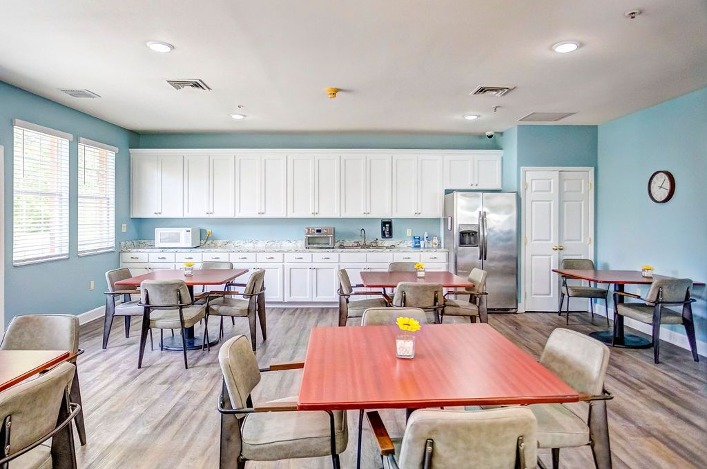 Dining room with red tables, chairs, white cabinets, and stainless steel refrigerator. Light blue walls and wood-look flooring.