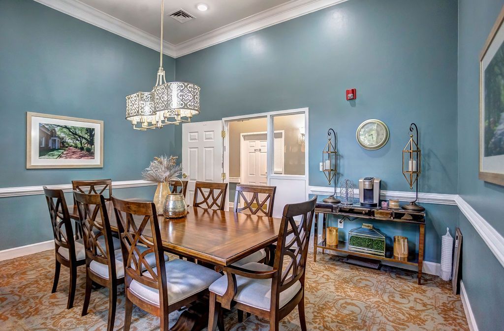 Formal dining room with large table, chairs, chandelier, and a buffet with coffee. Blue walls, floral carpet.