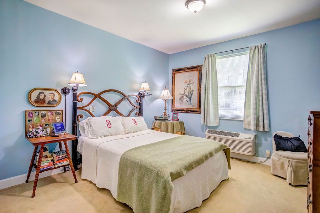 Bedroom with light blue walls, a bed with a decorative headboard, and a small table with a lamp.