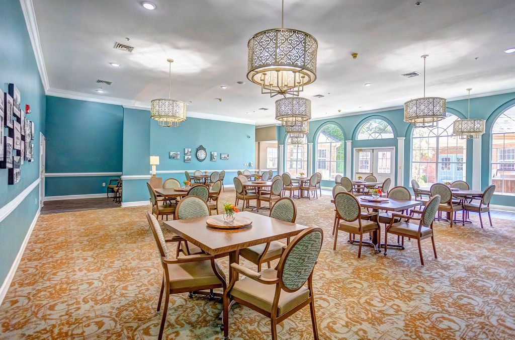 Dining room with tables, chairs, and ornate light fixtures. Blue walls, patterned carpet, and large windows.