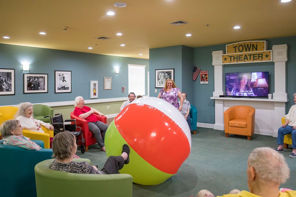 People in a community center play with a large beach ball near a TV and theater sign.