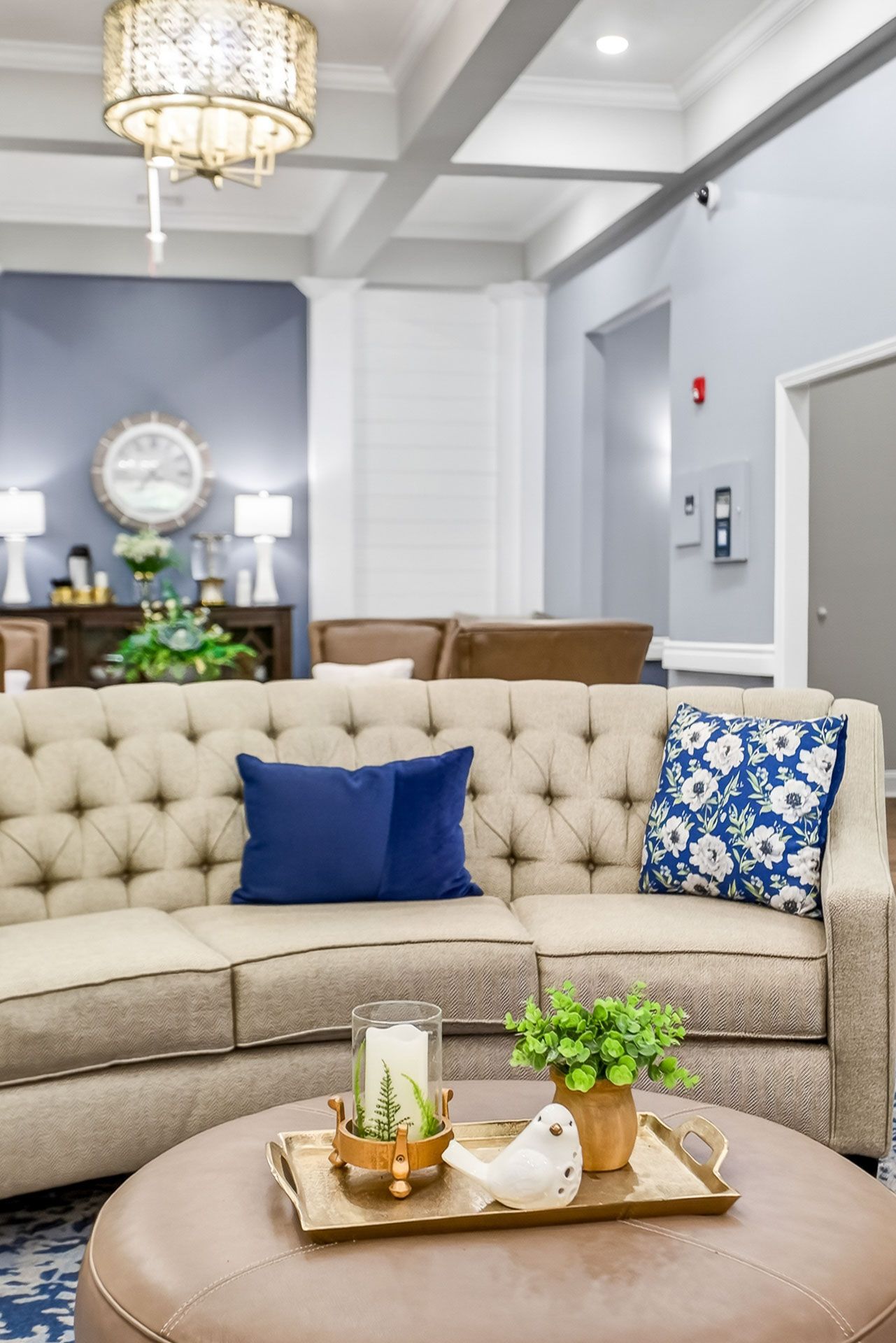Elegant living room with tufted beige sofa, blue pillows, round coffee table, and chandelier lighting
