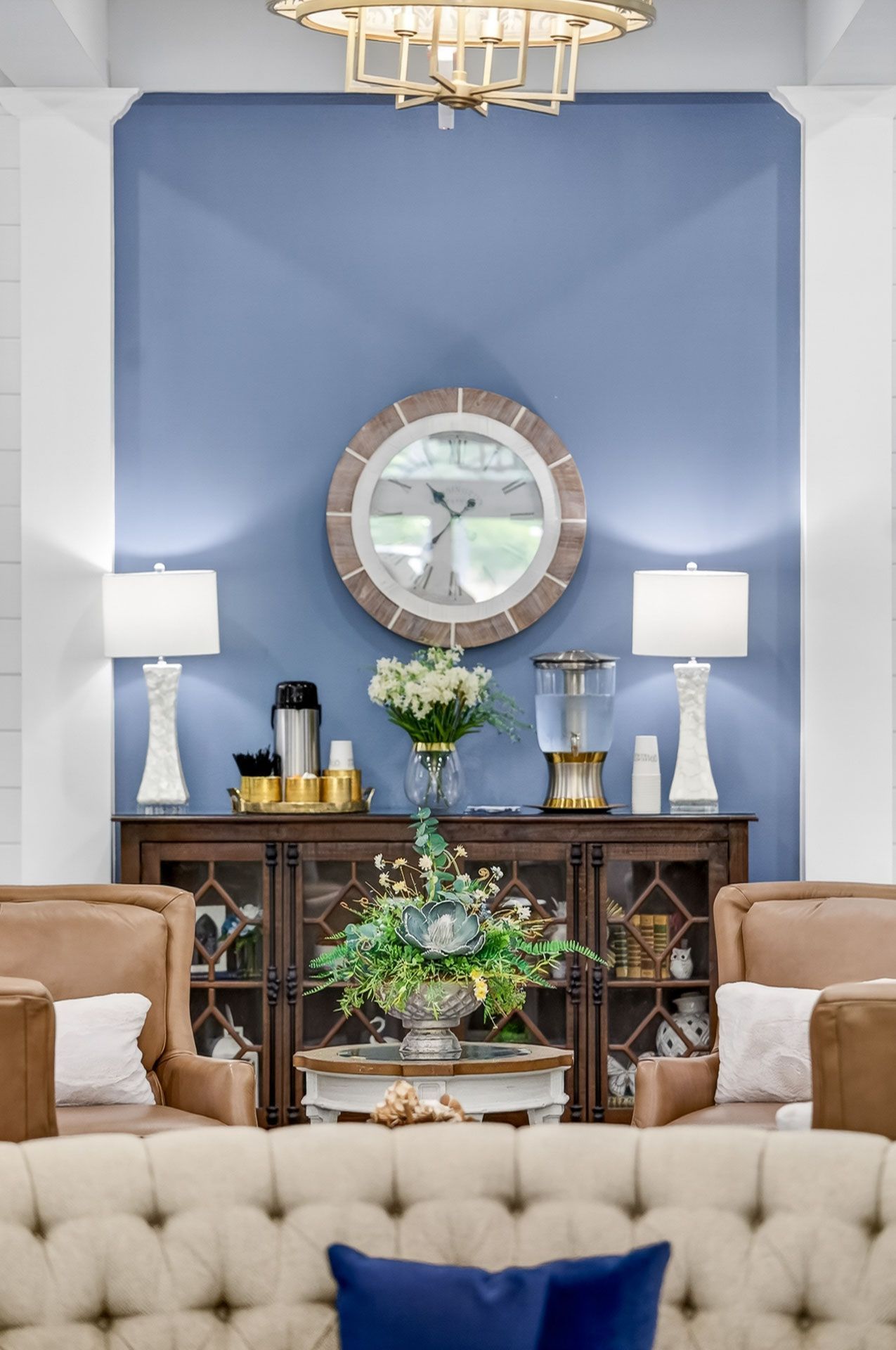 Elegant living room with blue accent wall, round clock, lamps, wooden sideboard, and tufted sofa