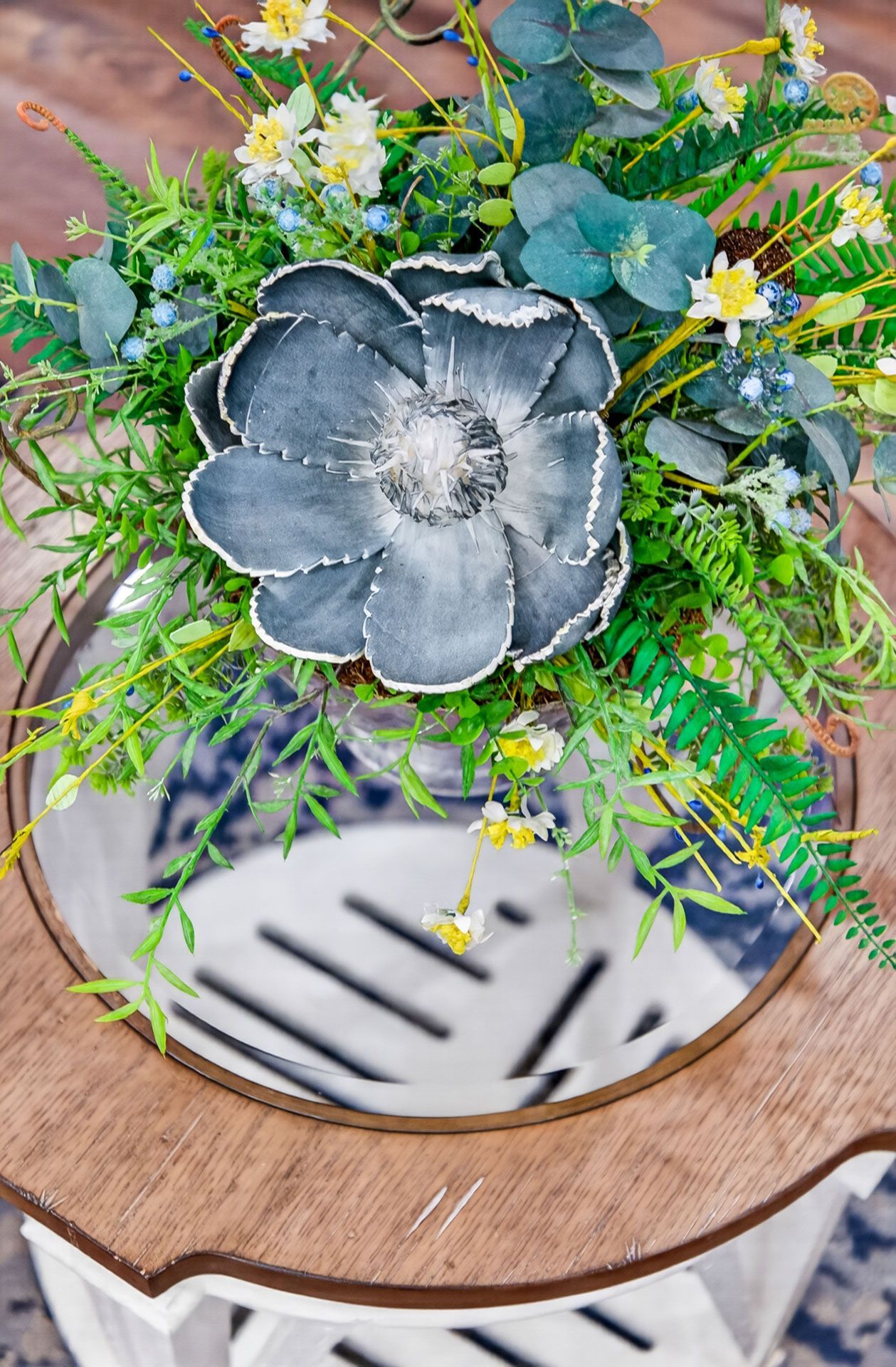 Floral centerpiece with gray flower and greenery in a round striped vase on a wooden table