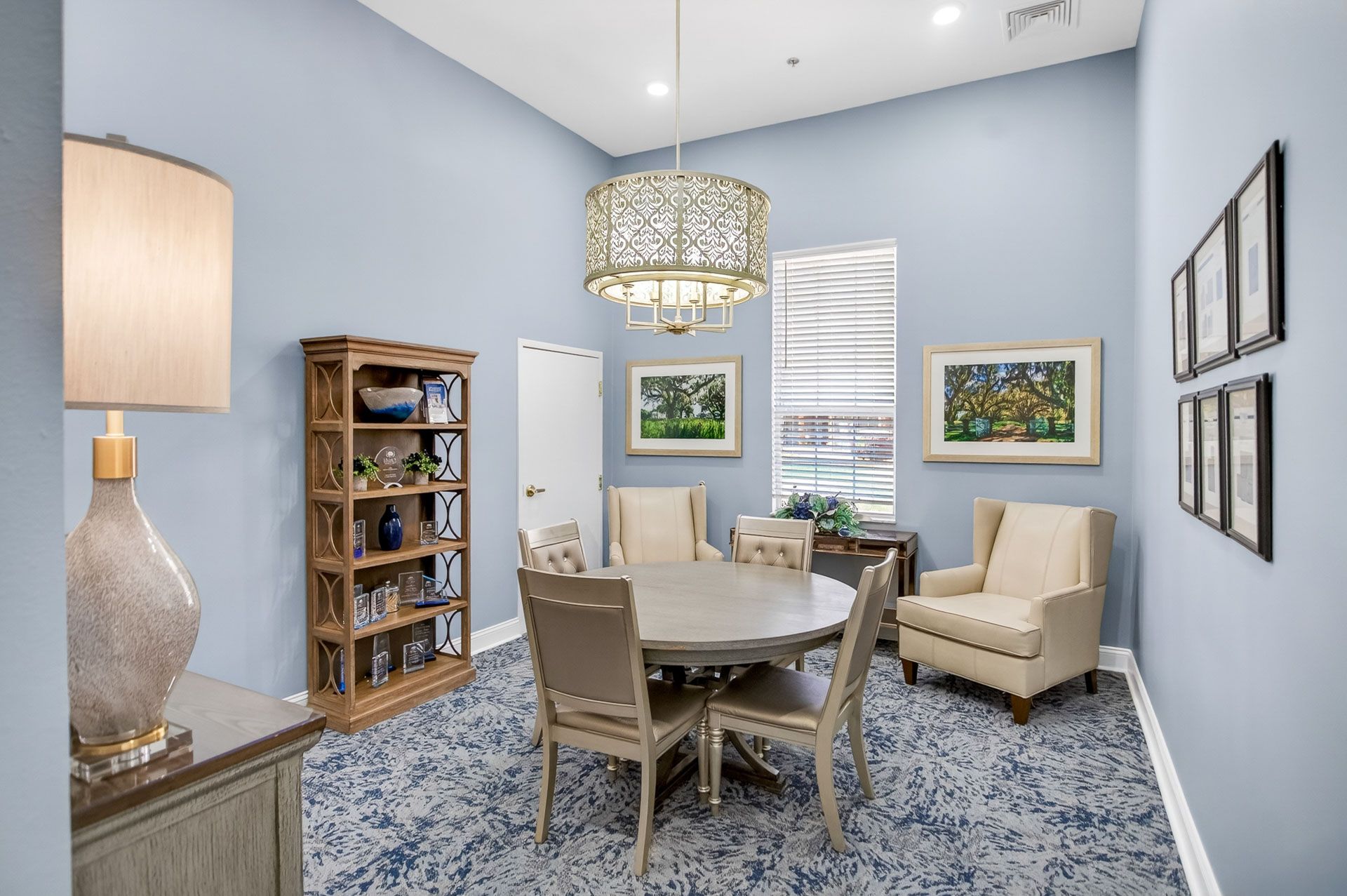 Bright home office with dining table, cream chairs, blue walls, patterned carpet, and hanging chandelier.