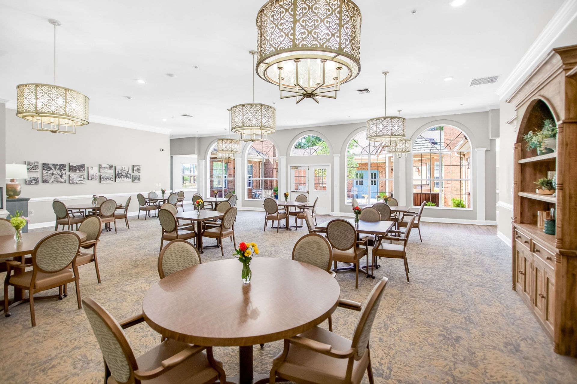 Bright dining room with round tables, wicker chairs, chandeliers, and large arched windows