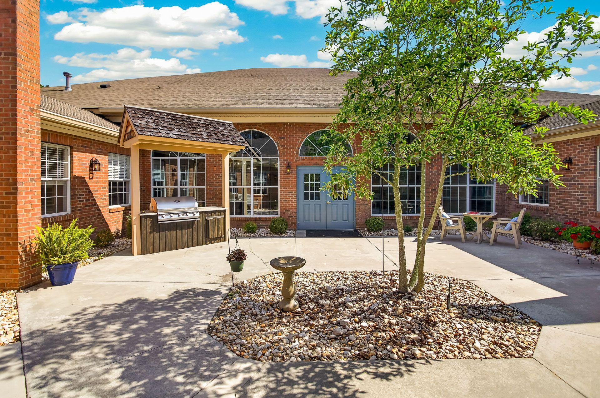 Courtyard with brick buildings, a patio, and a tree in the center under a blue sky