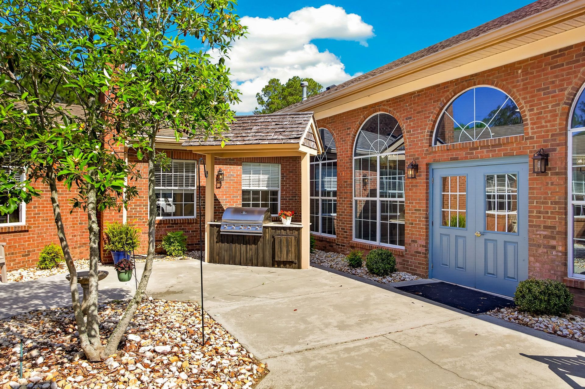 Brick building entrance with arched windows, blue doors, and a tree-lined concrete walkway