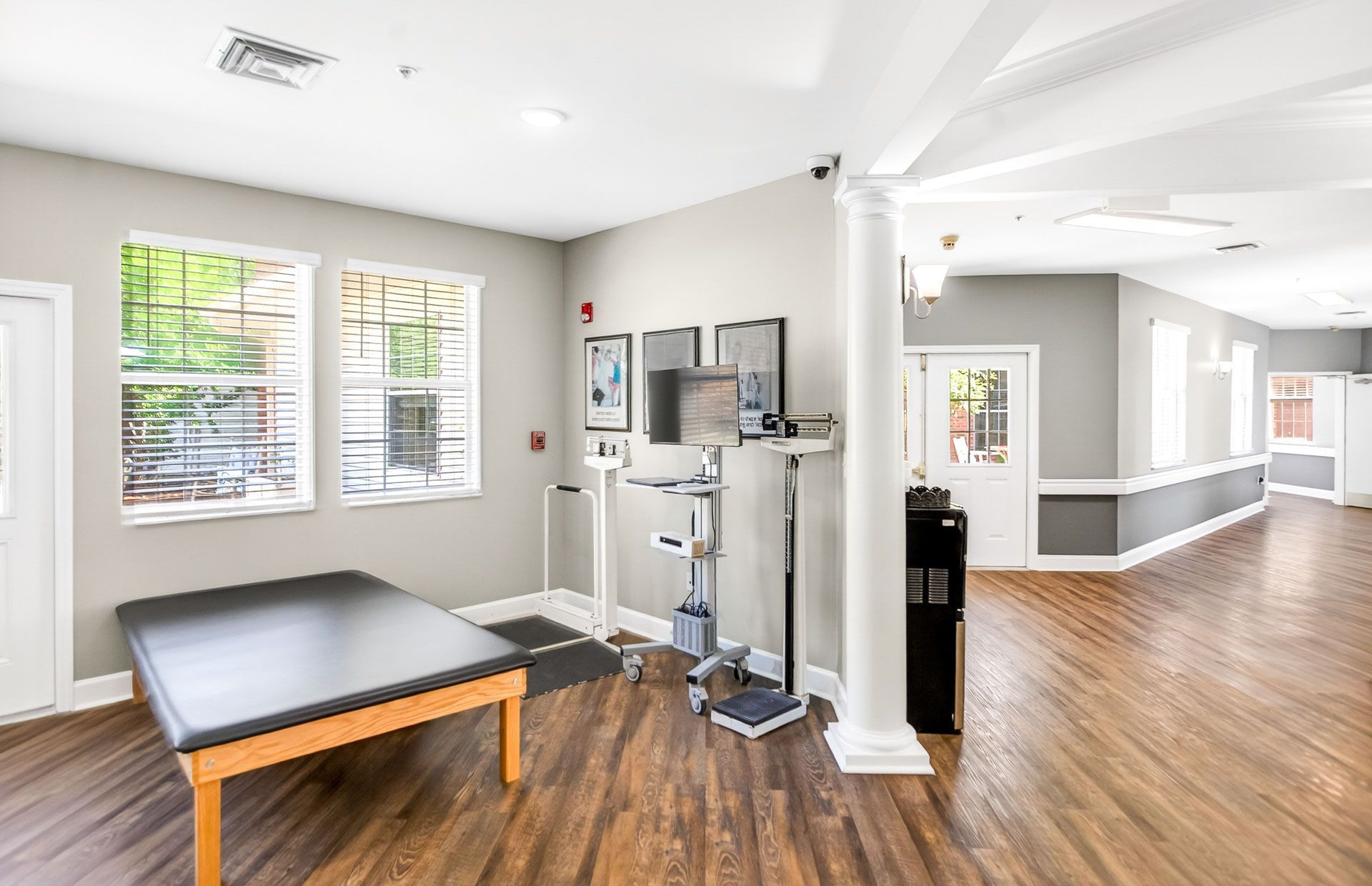 Bright chiropractic treatment room with exam table, exercise equipment, and hardwood floors