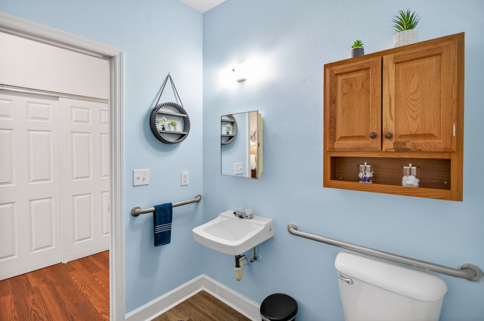 Accessible bathroom with blue walls, white sink, grab bars, and toilet paper cabinet.