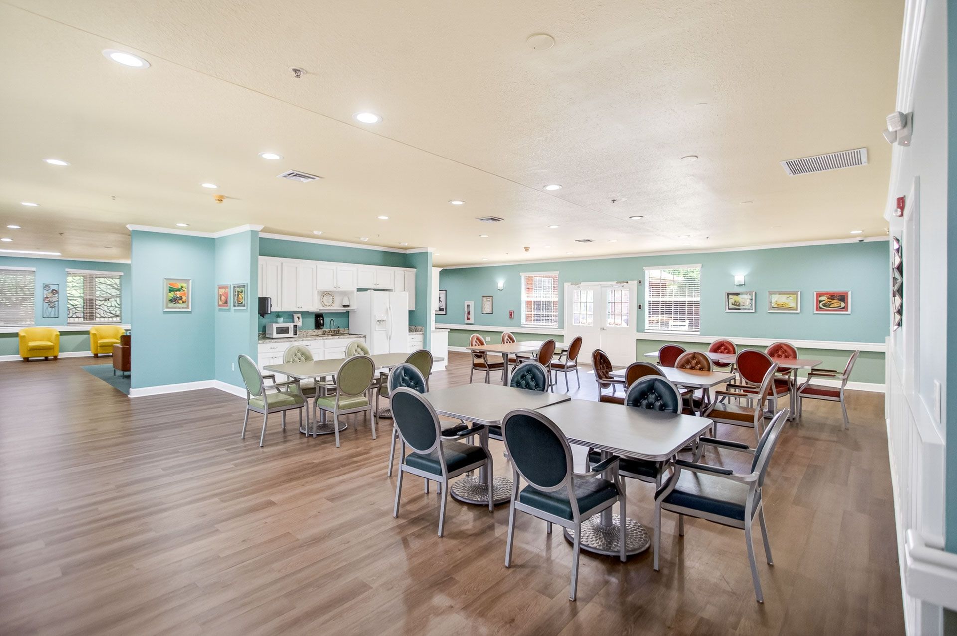 Bright community dining room with round tables, chairs, light blue walls, and wood flooring
