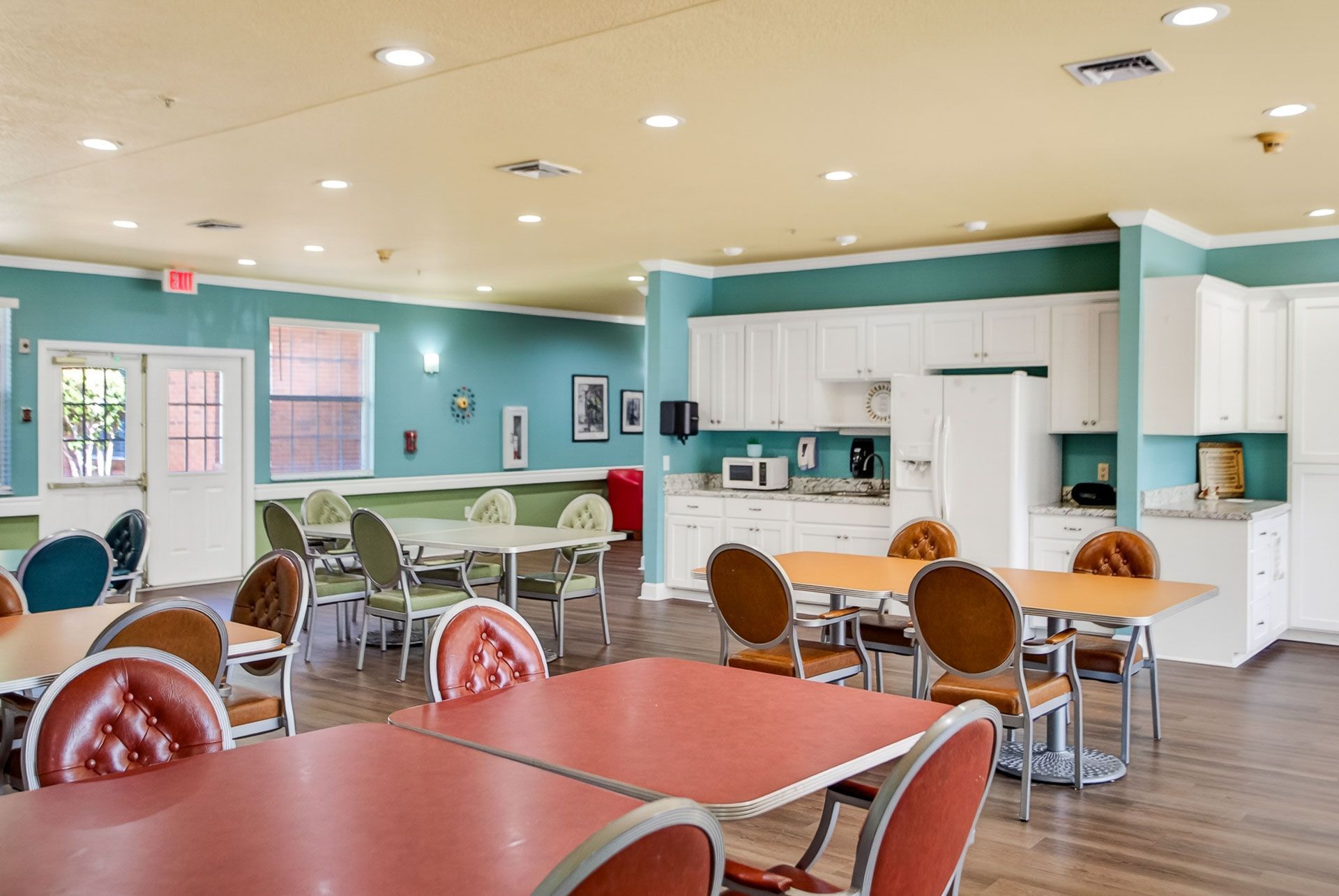 Bright café dining area with red and brown tables, teal walls, and a white counter and kitchen area