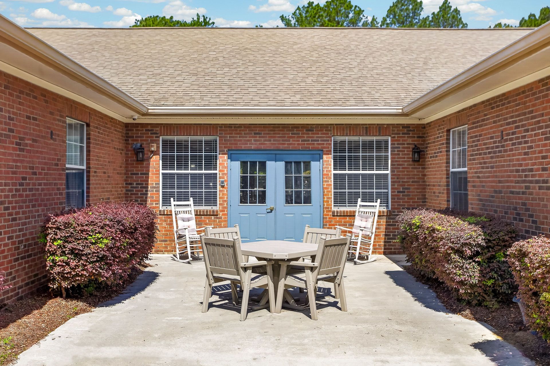 Patio seating area outside a brick building with blue double doors and white chairs around a table