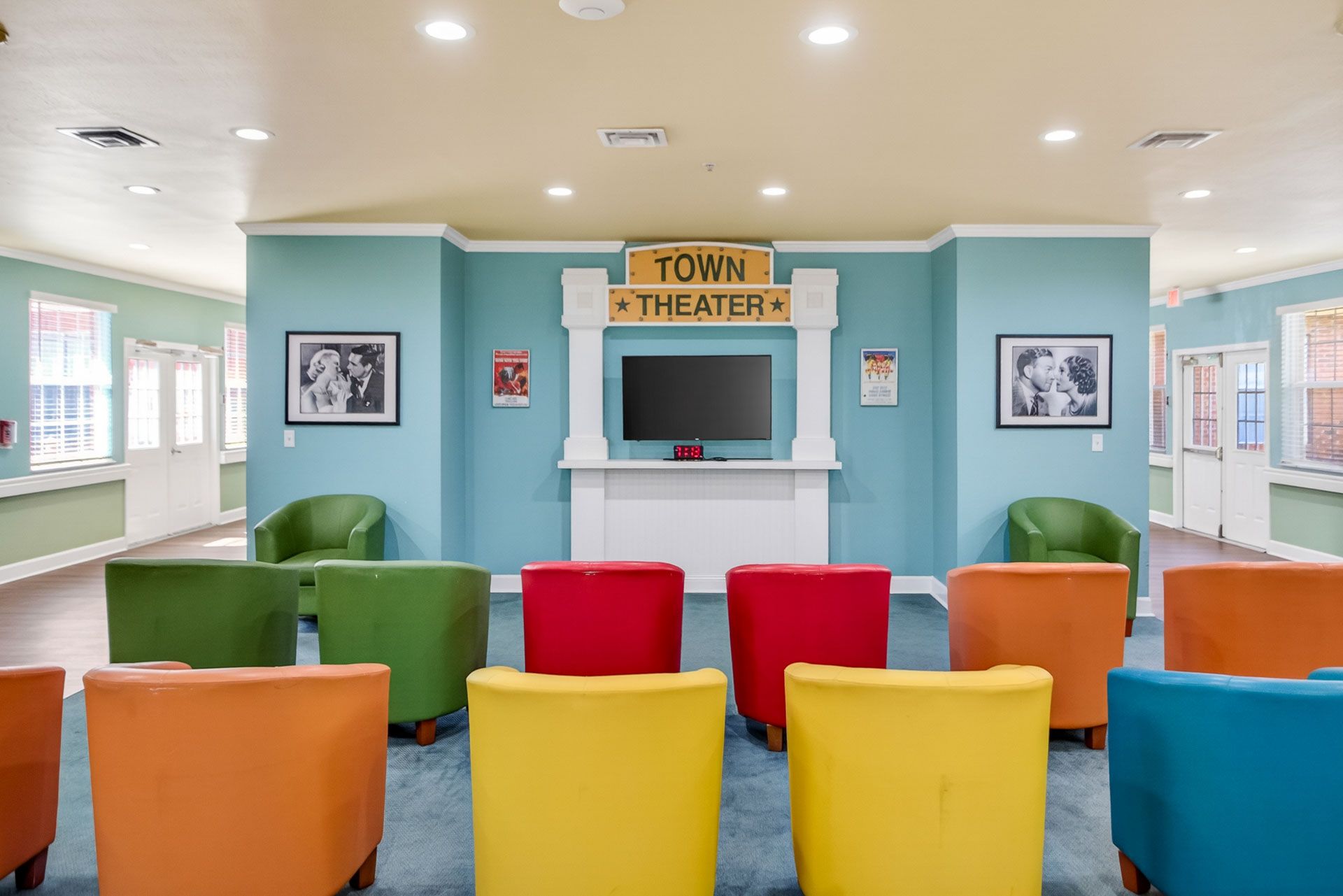 Colorful chairs in a bright waiting room with a TV and wall art, centered on a teal reception area.