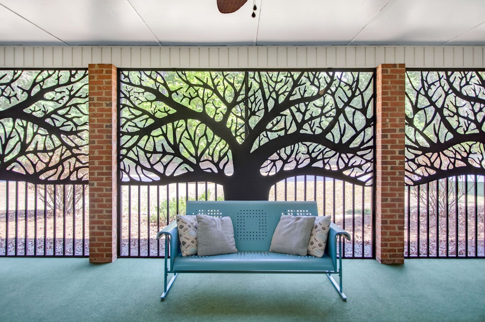 Blue bench with patterned pillows in front of a brick wall and tree mural with fence backdrop