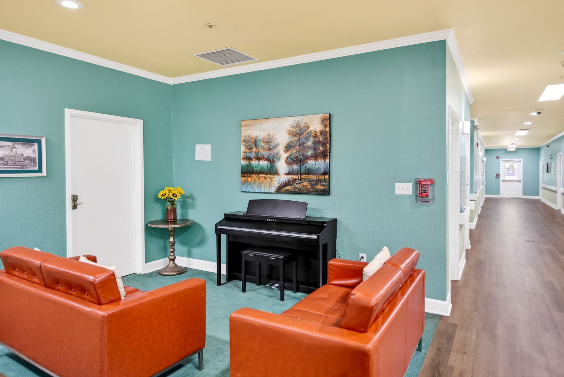 Lobby lounge with orange chairs, black piano, teal walls, and a hallway leading back