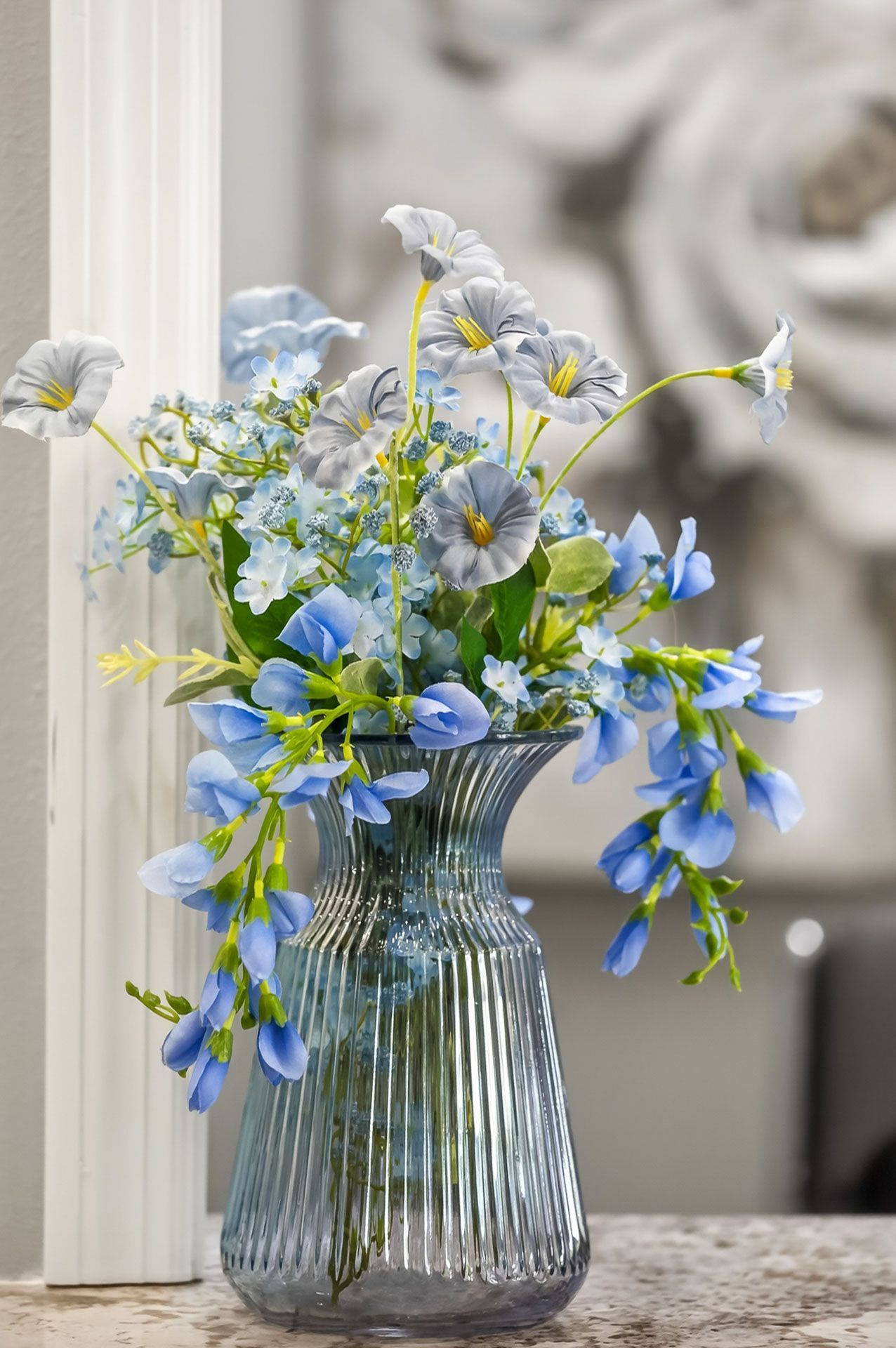 Blue and white flowers in a clear glass vase on a table by a window