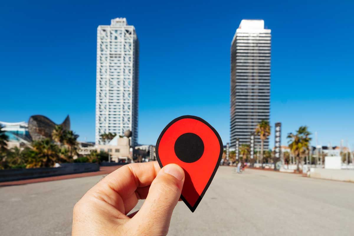 A person is holding a red pin in front of a city.