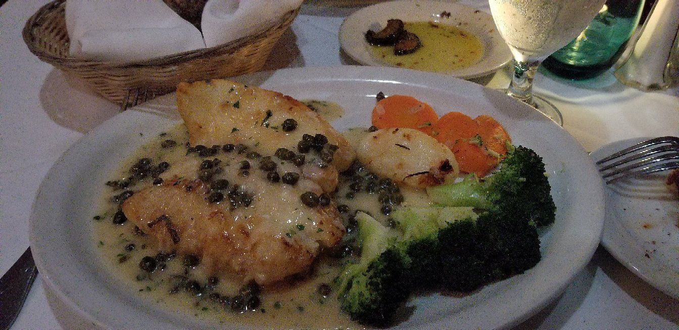 A plate of food with broccoli , carrots and scallops on a table.