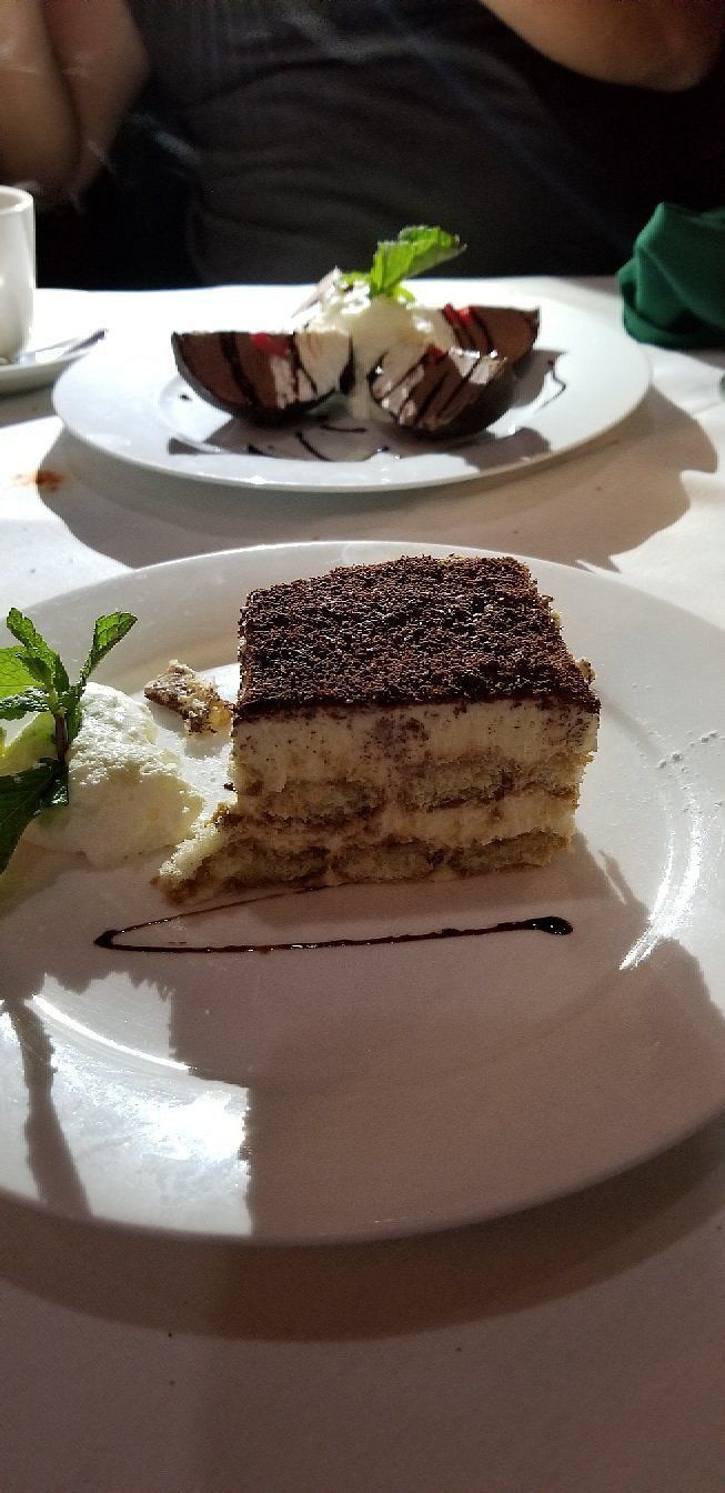 A slice of tiramisu is on a plate next to a plate of dessert.