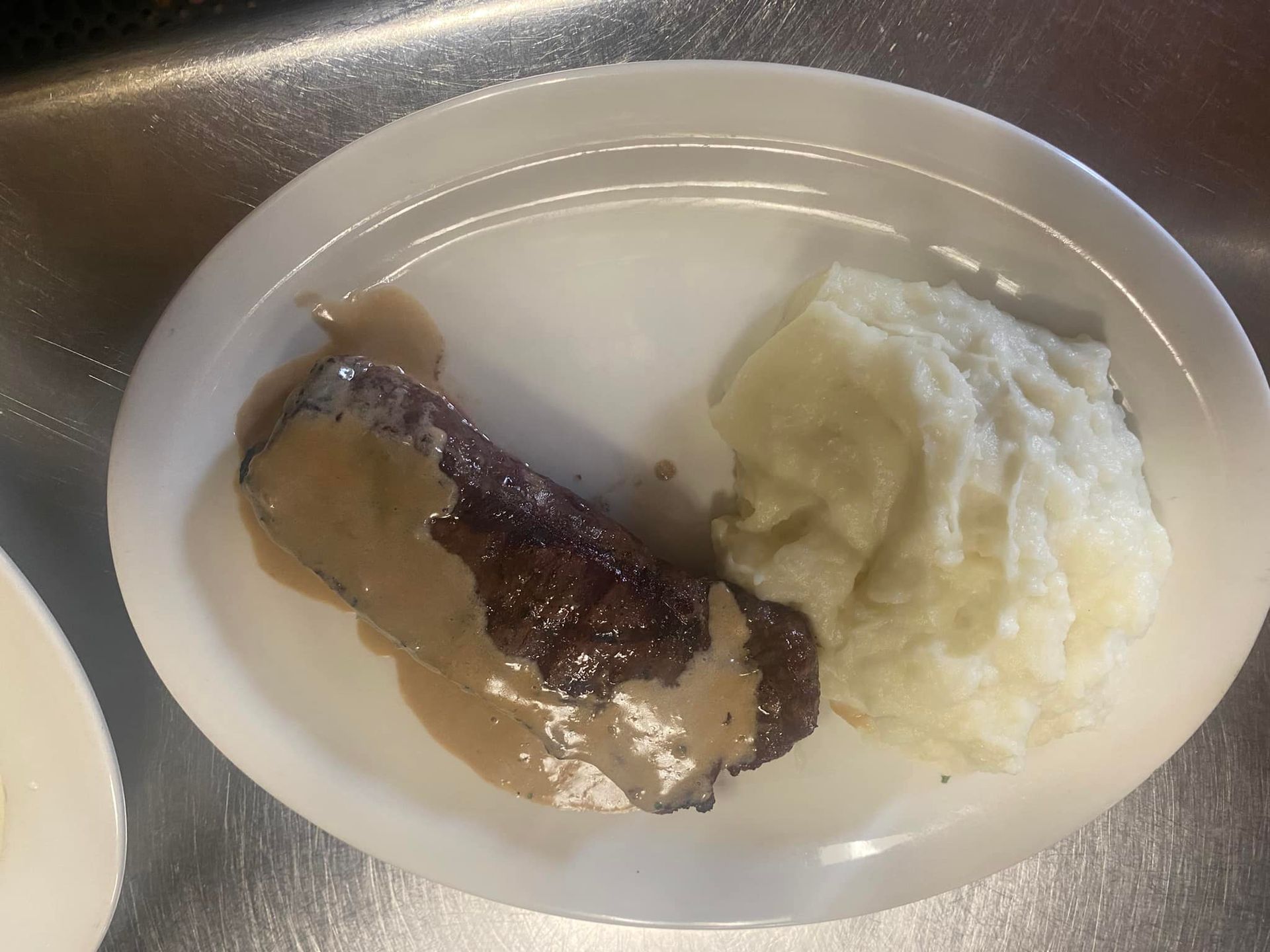 A white plate topped with meat and mashed potatoes on a counter.