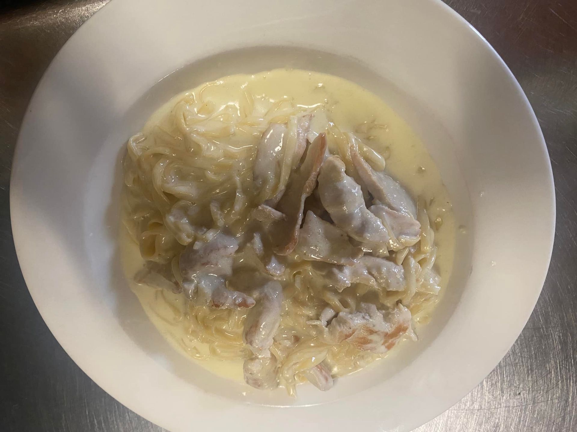 A white bowl filled with noodles and sauce on a table.