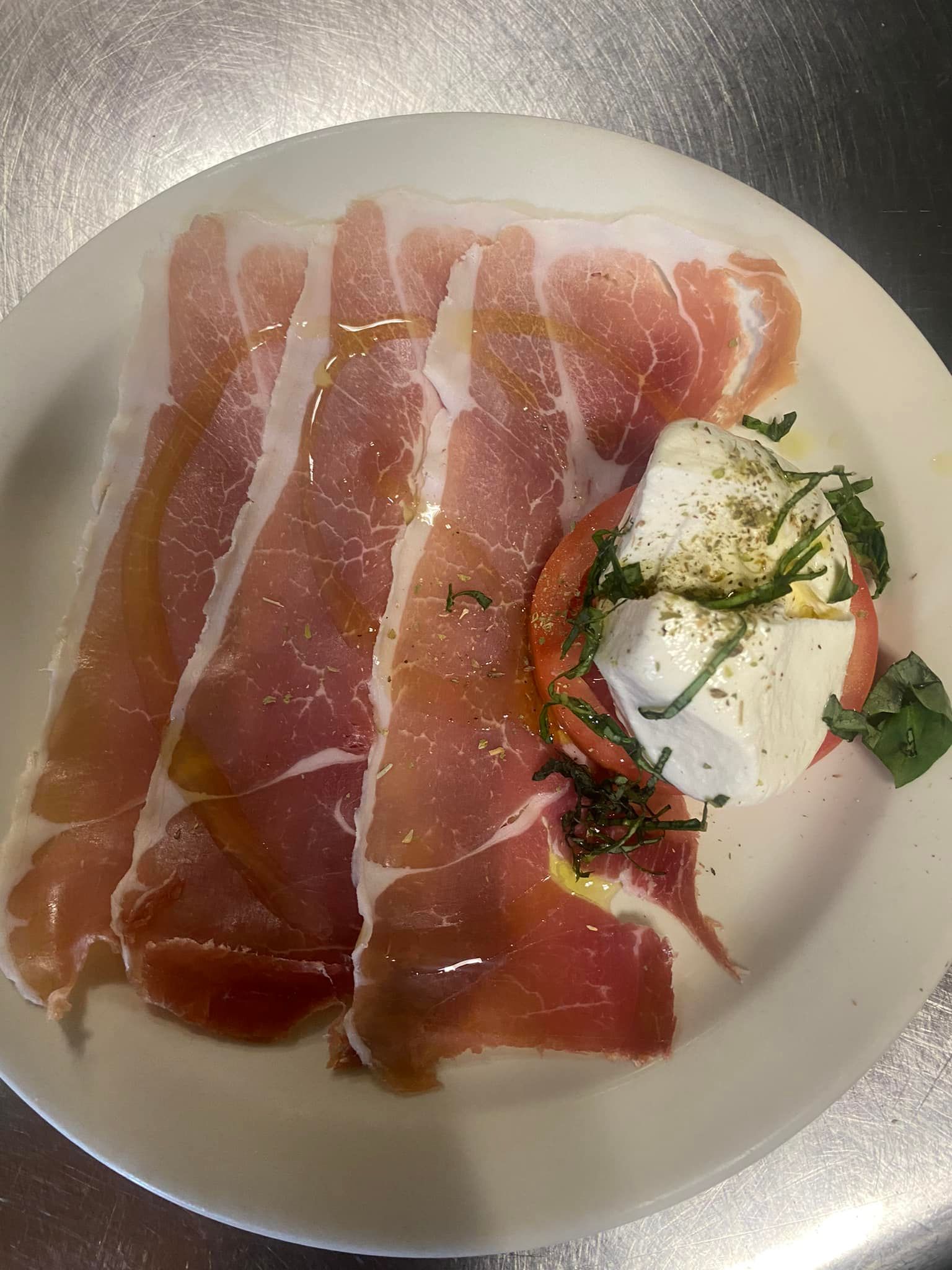 A white plate topped with ham , mozzarella and tomatoes.