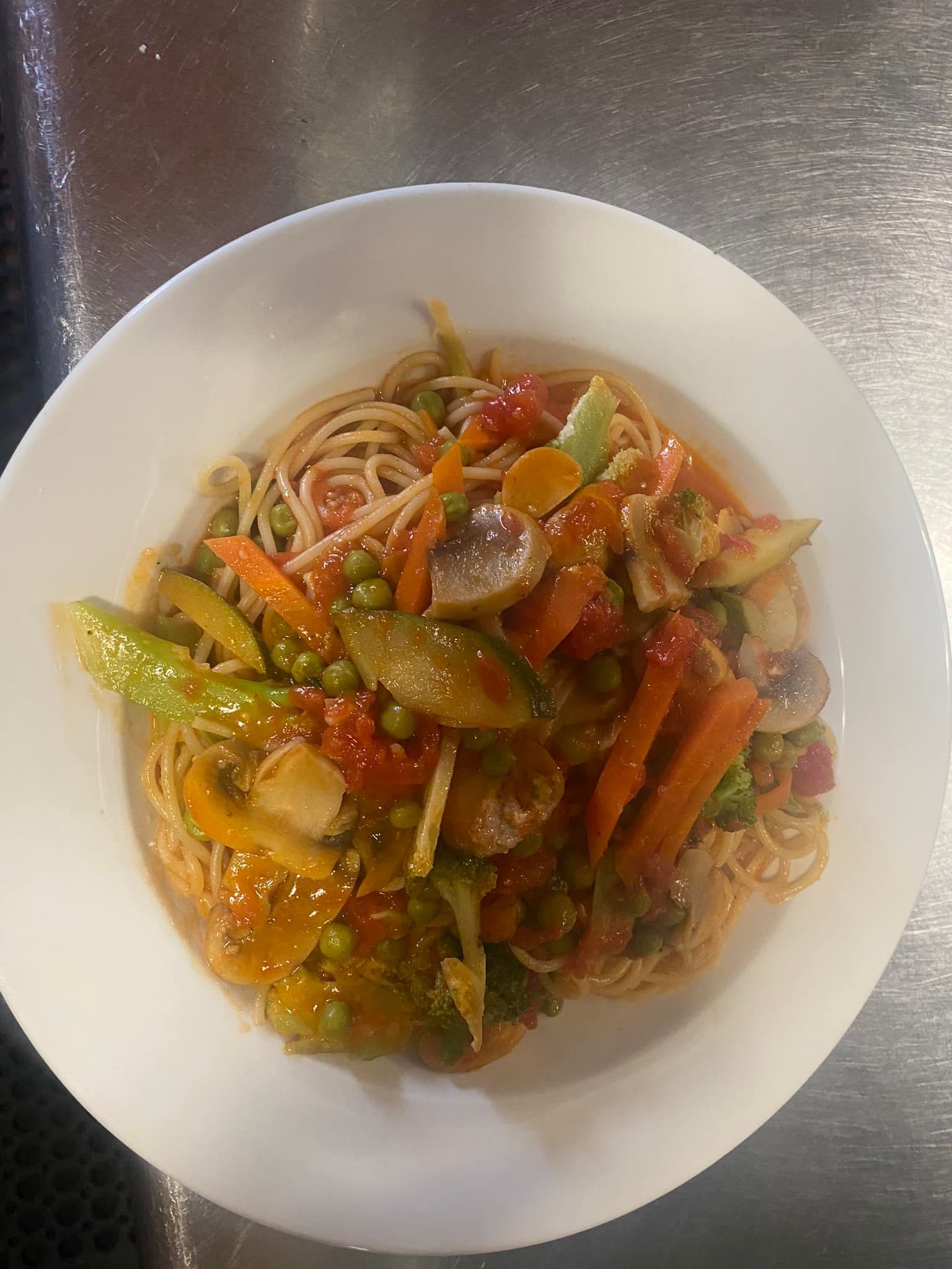 A white plate topped with spaghetti and vegetables on a table.
