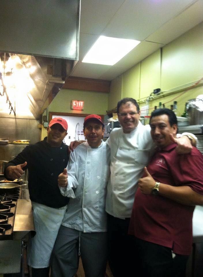 Four men are posing for a picture in a kitchen with an exit sign in the background