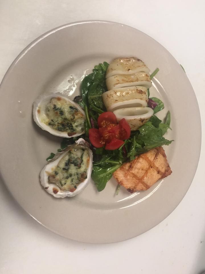 A plate of food with oysters , squid , and salmon on a table.
