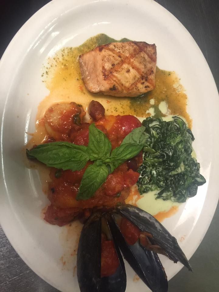 A white plate topped with a piece of meat spinach and mussels