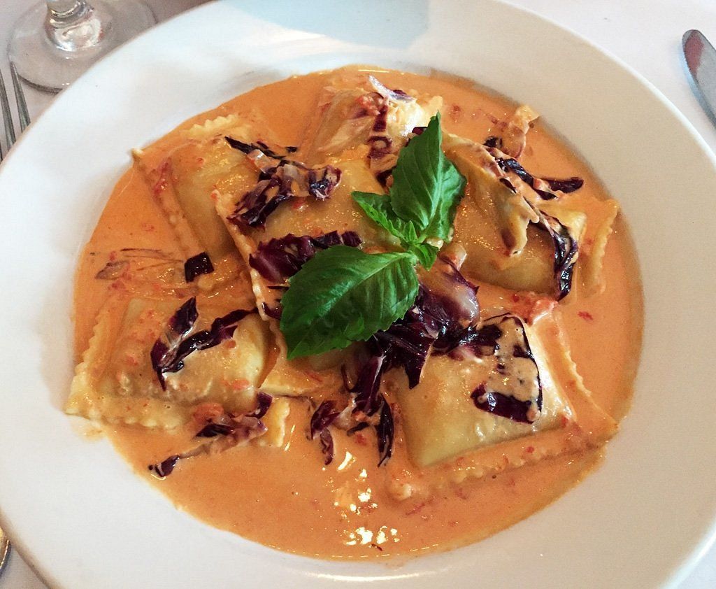 A white plate topped with ravioli and sauce on a table.