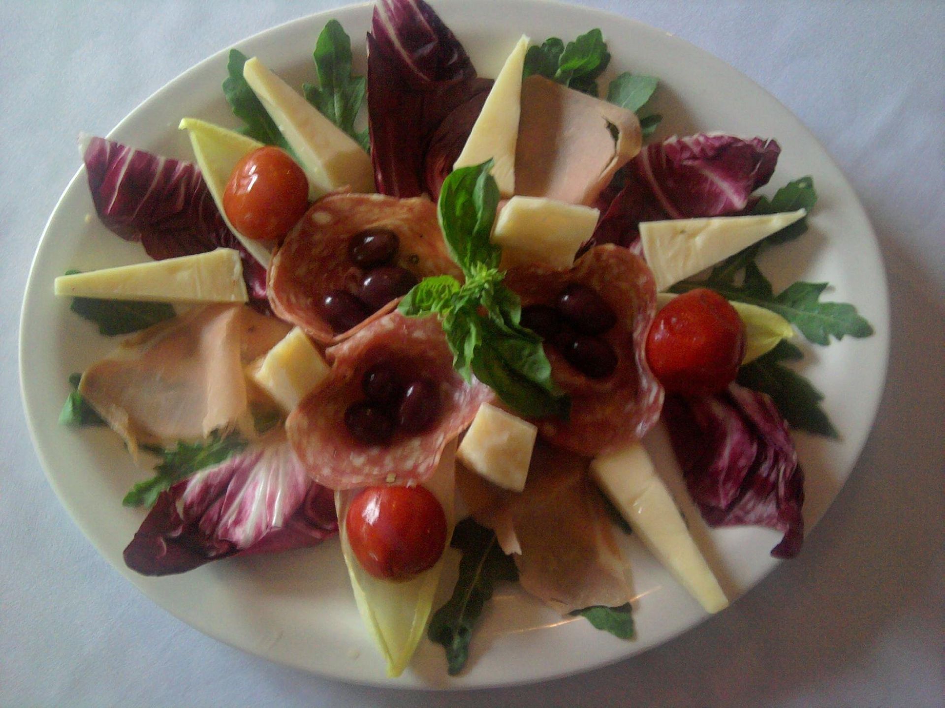 A white plate topped with meats cheeses and tomatoes