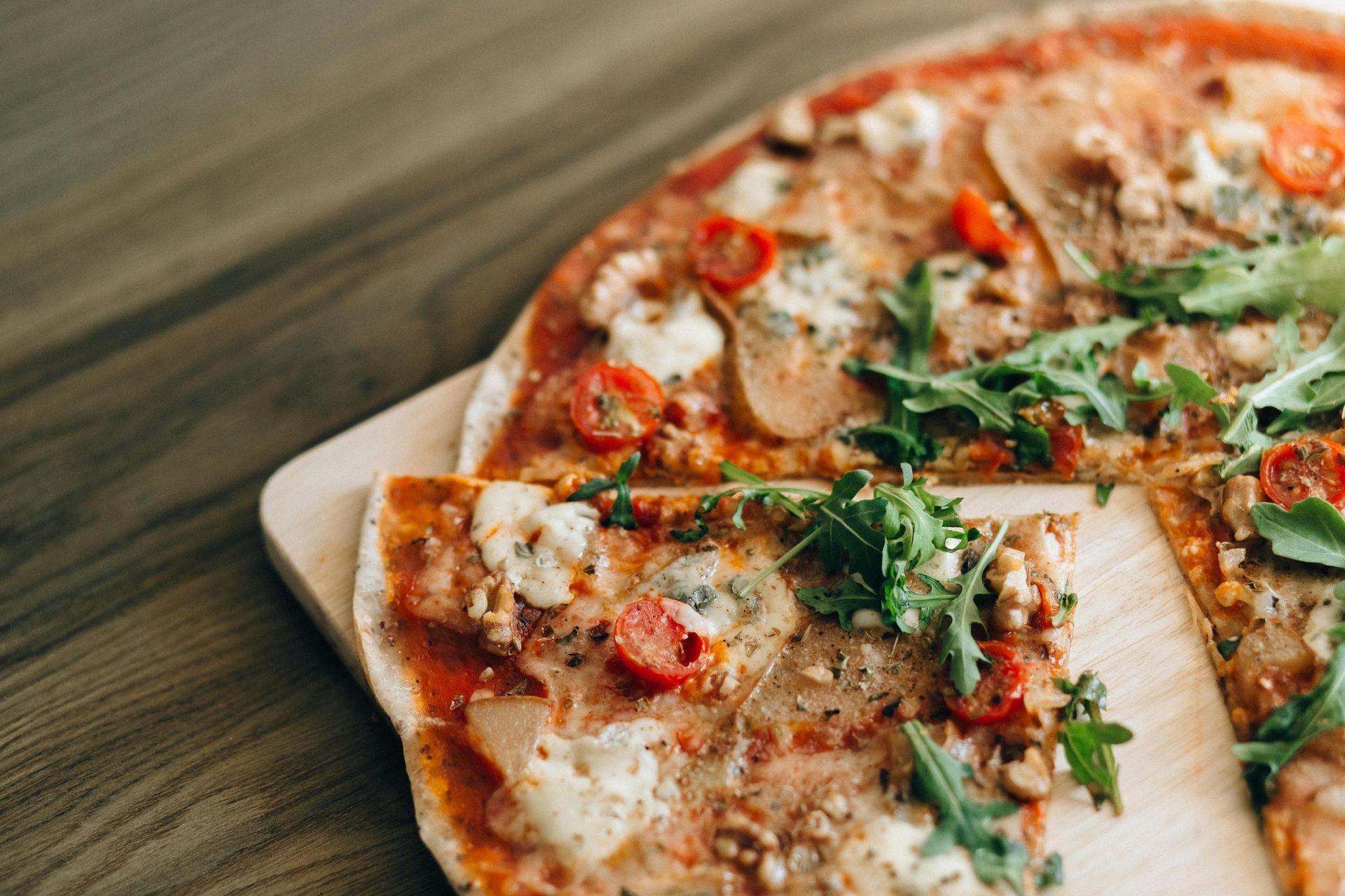 A pizza is sitting on a wooden cutting board on a wooden table.
