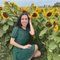 A woman in a green dress is sitting in a field of sunflowers.