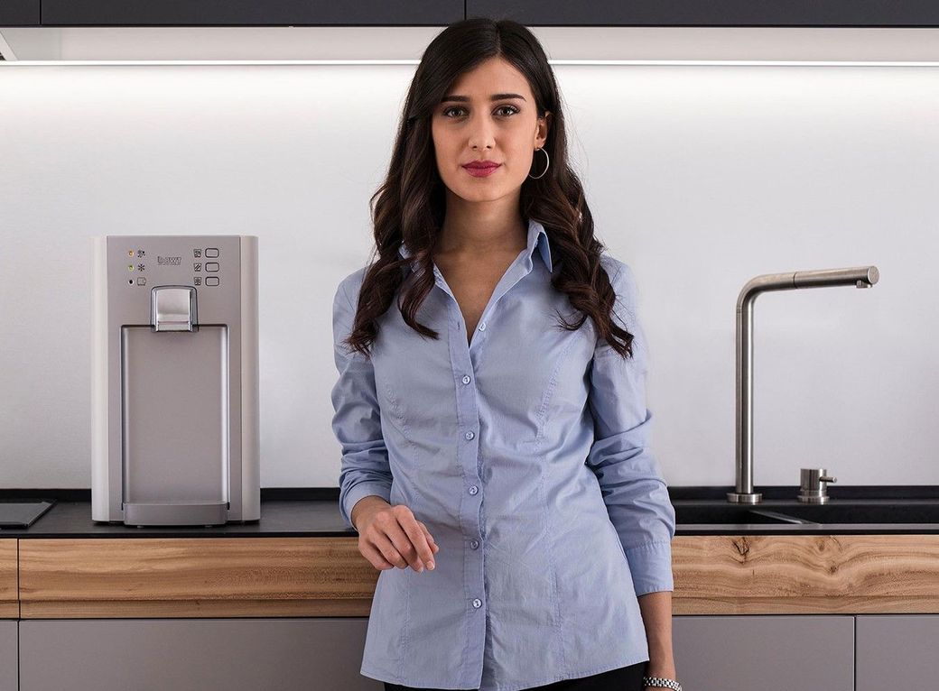 Una donna con una camicia blu è in piedi in cucina accanto a un lavandino.